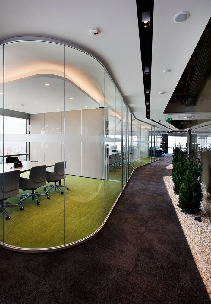 Curved floor-to-ceiling glass meeting room along a landscaped corridor