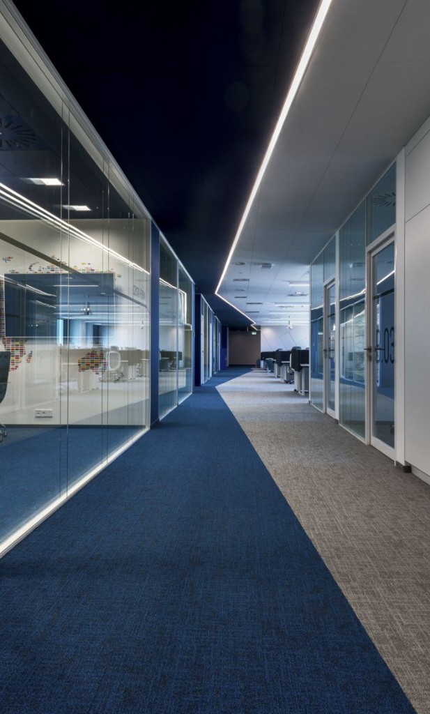 Deep office corridor with clear glass partitions and linear lighting
